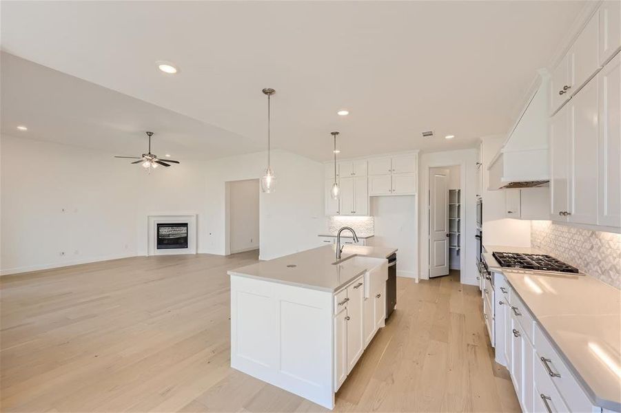 Kitchen featuring ceiling fan, light hardwood / wood-style floors, a center island with sink, backsplash, and white cabinetry