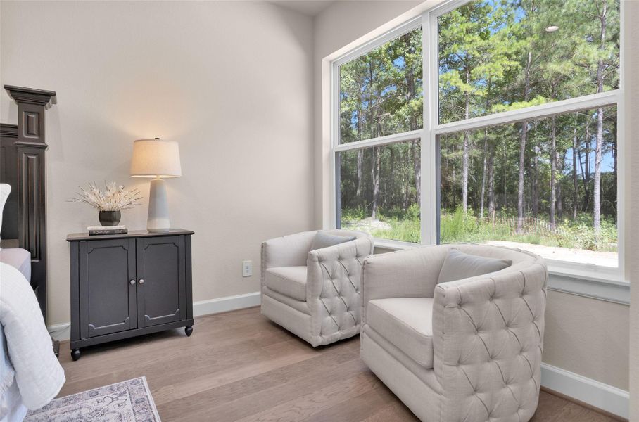 Tucked into a sunny corner of the primary suite, this cozy sitting area offers the perfect spot to relax with peaceful views of the surrounding trees just beyond the oversized windows.