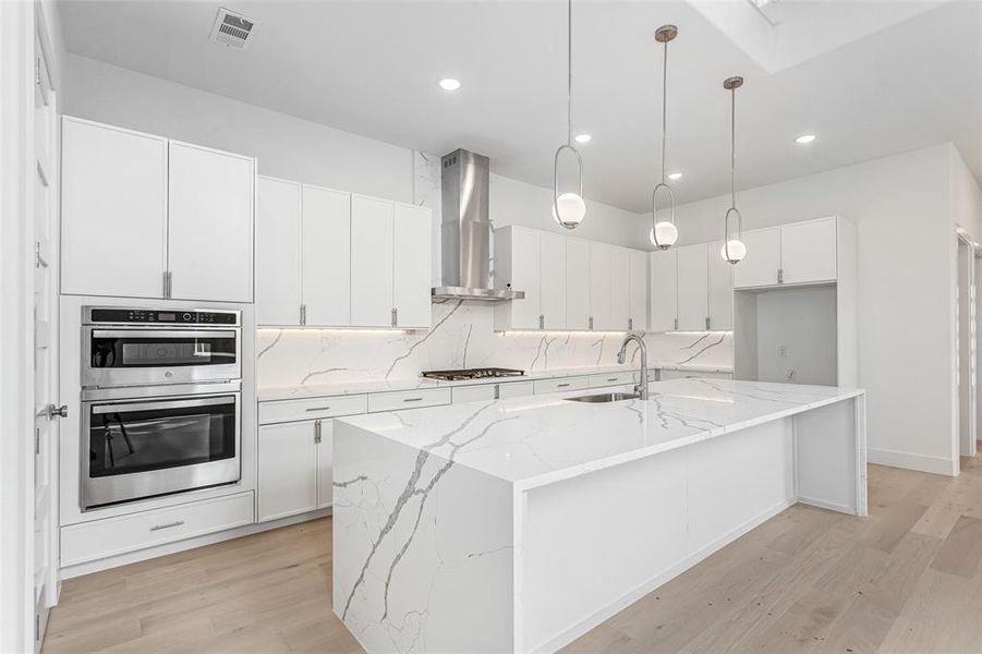 Kitchen featuring wall chimney exhaust hood, stainless steel appliances, a sink, light wood-style floors, and white cabinets