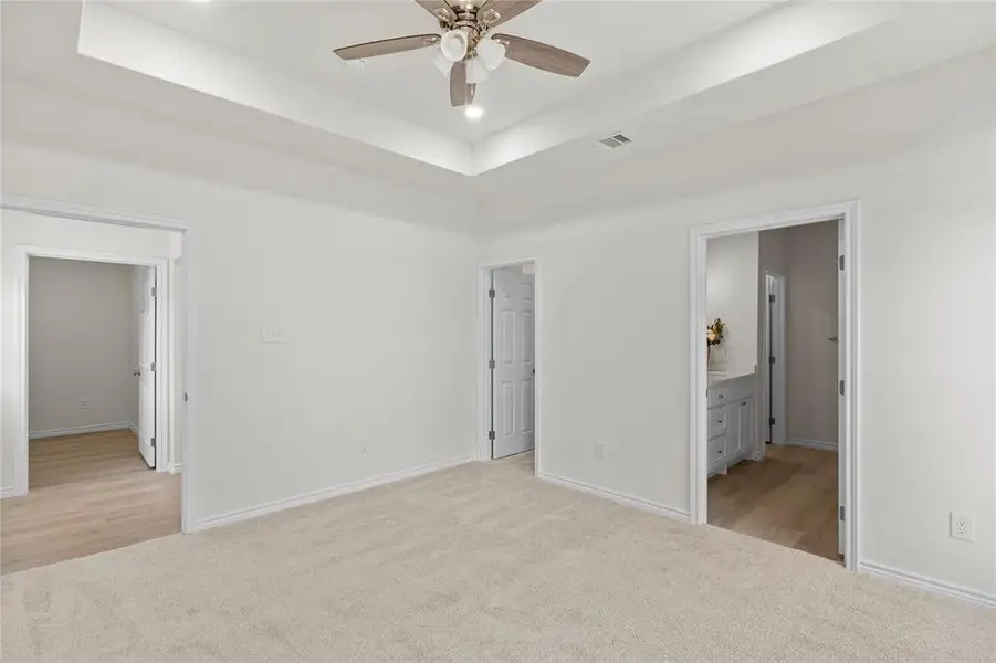 Unfurnished bedroom with a tray ceiling, light colored carpet, recessed lighting, ceiling fan, and ensuite bath Unfurnished bedroom with a tray ceiling, light colored carpet, recessed lighting, ceiling fan, and ensuite bath