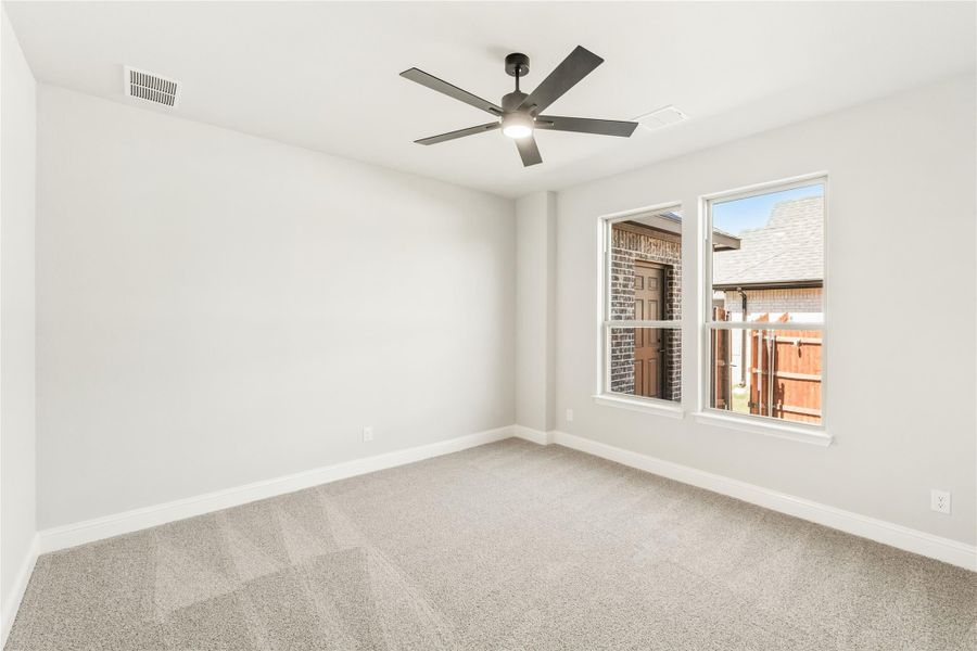 Empty bedroom with carpet flooring, ceiling fan, and a window overlooking neighboring homes Empty bedroom with carpet flooring, ceiling fan, and a window overlooking neighboring homes