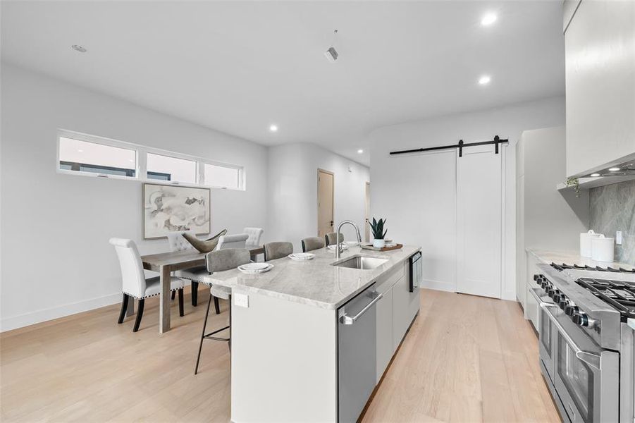 Kitchen featuring a barn door, a kitchen breakfast bar, stainless steel appliances, a center island with sink, and light wood-style floors
