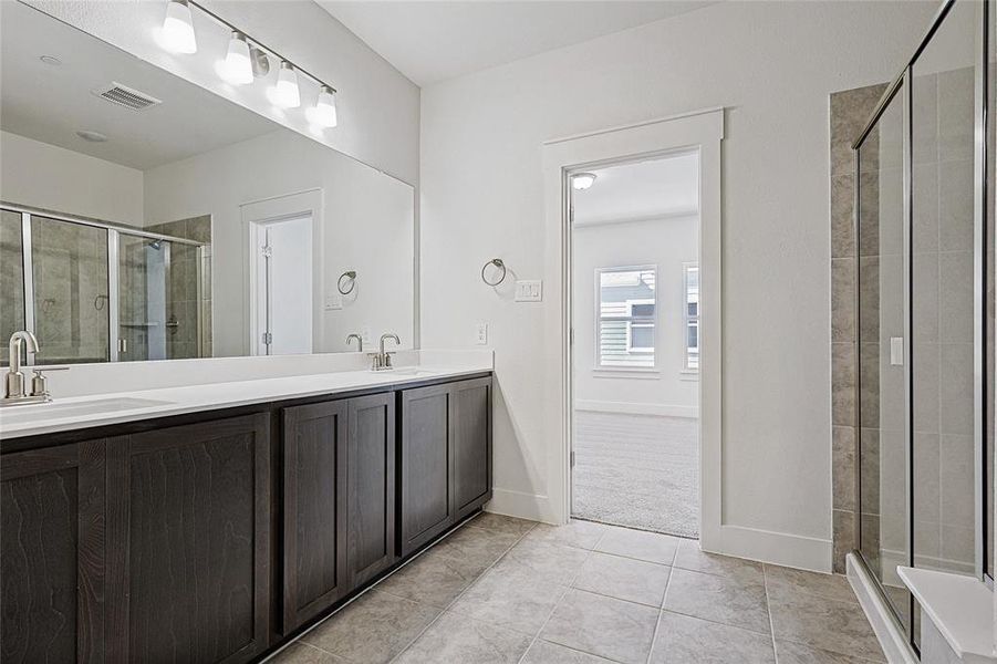 Bathroom with a shower stall, double vanity, and light tile patterned floors