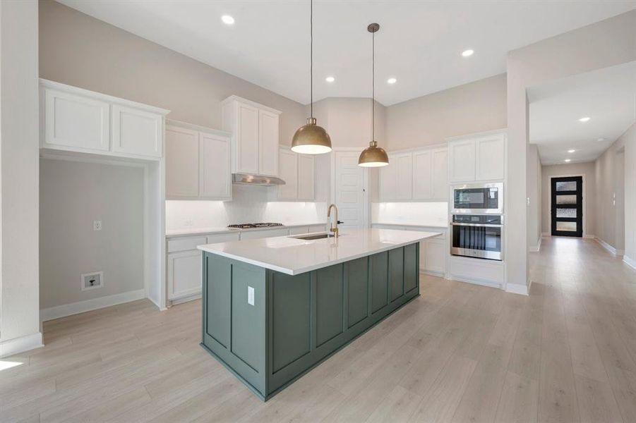 Open-concept kitchen featuring a large central island with a sage green finish and a light-toned countertop, white cabinetry with under-cabinet lighting, a built-in stainless steel double oven, and recessed lighting