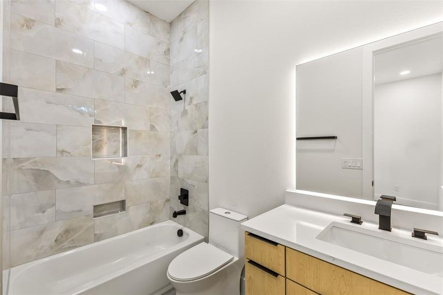 Contemporary bathroom featuring a tub/shower combination with tiled surround, a built-in shower niche, a floating wood-finish vanity with a white countertop, and an illuminated mirror