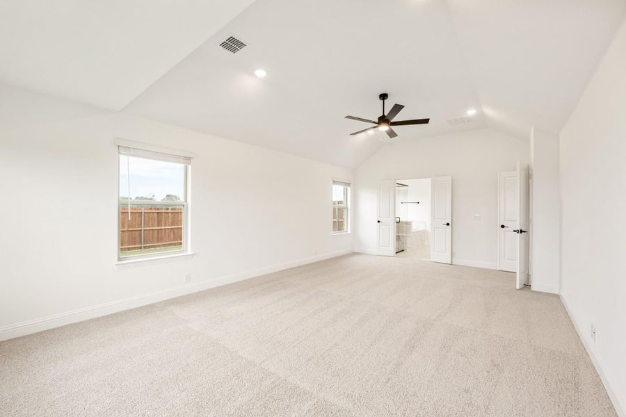 Spacious bedroom with vaulted ceiling, ceiling fan, carpet flooring, and attached bathroom