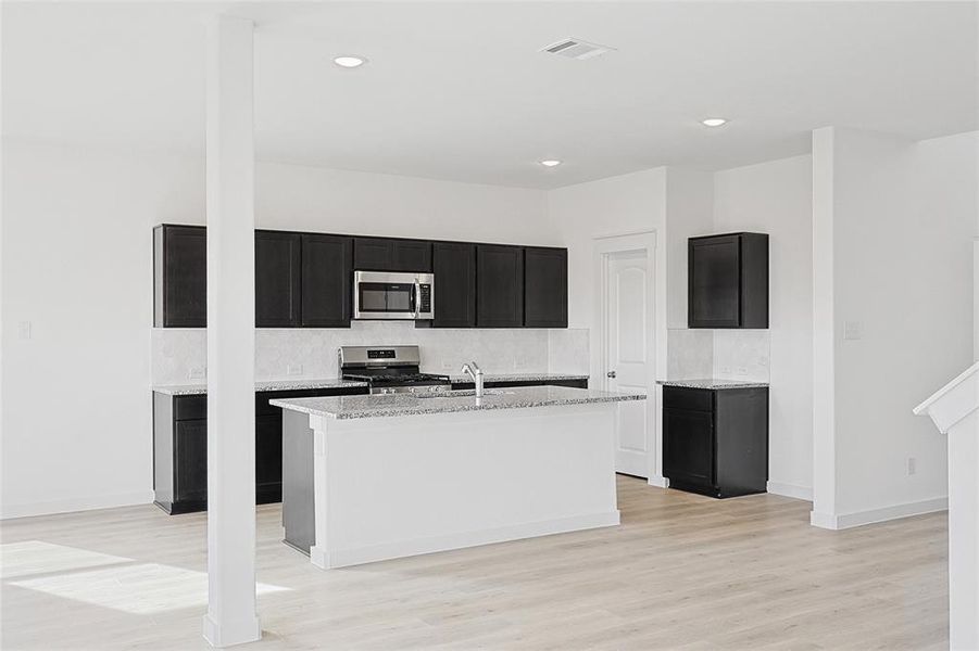 Kitchen with a center island with sink, light hardwood / wood-style flooring, appliances with stainless steel finishes, tasteful backsplash, and light stone counters