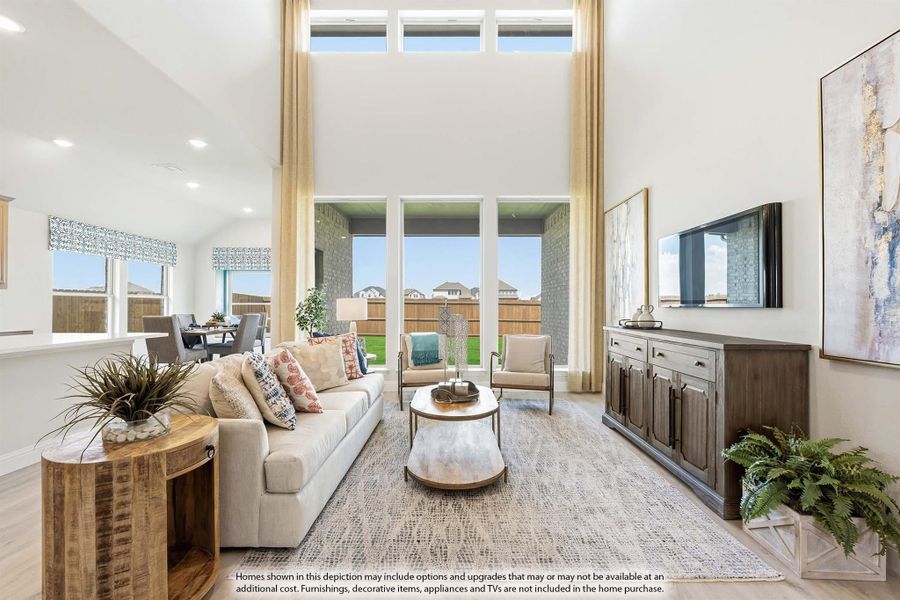 Living room with two-story ceilings, tall windows, neutral sofa, and wood media console with wall-mounted TV