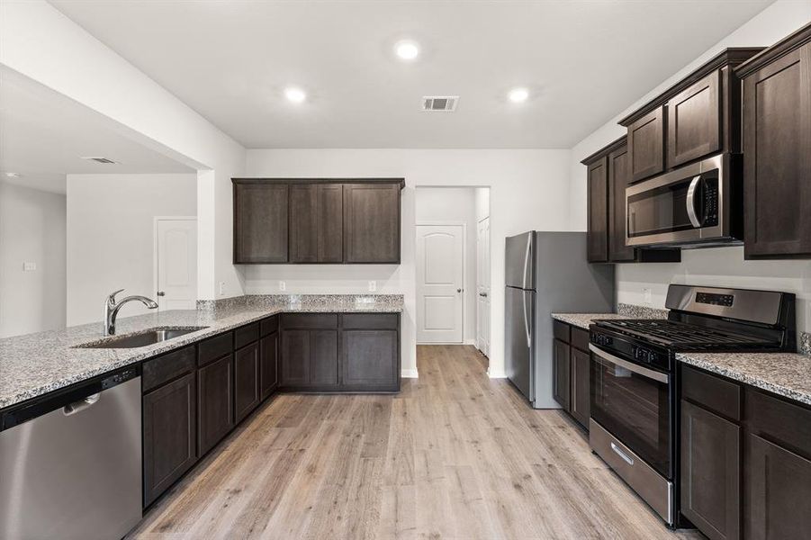 Kitchen with light wood-type flooring, appliances with stainless steel finishes, light stone countertops, and sink