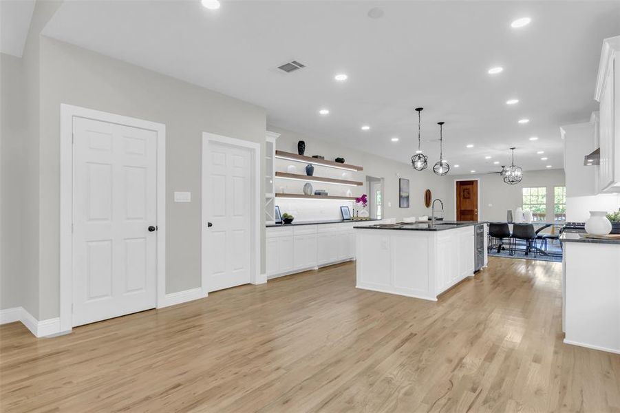 Kitchen with open shelves, white cabinetry, recessed lighting, hanging light fixtures, and a kitchen island with sink