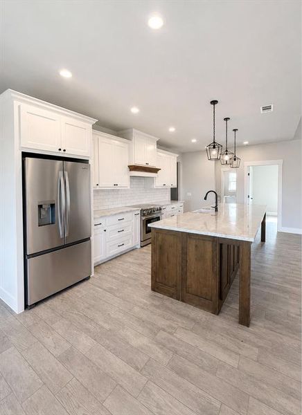 Expansive kitchen featuring a large island with a substantial countertop, recessed lighting, wood-finish flooring, white cabinetry, and stainless steel appliances Expansive kitchen featuring a large island with a substantial countertop, recessed lighting, wood-finish flooring, white cabinetry, and stainless steel appliances