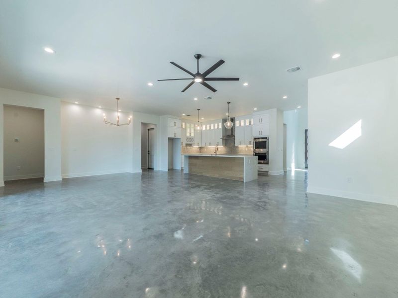 Unfurnished living room with a ceiling fan, concrete flooring, recessed lighting, and a chandelier Unfurnished living room with a ceiling fan, concrete flooring, recessed lighting, and a chandelier