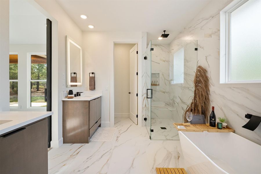 Full bathroom with a marble finish shower, a freestanding bath, two vanities, light marble finish floors, and recessed lighting