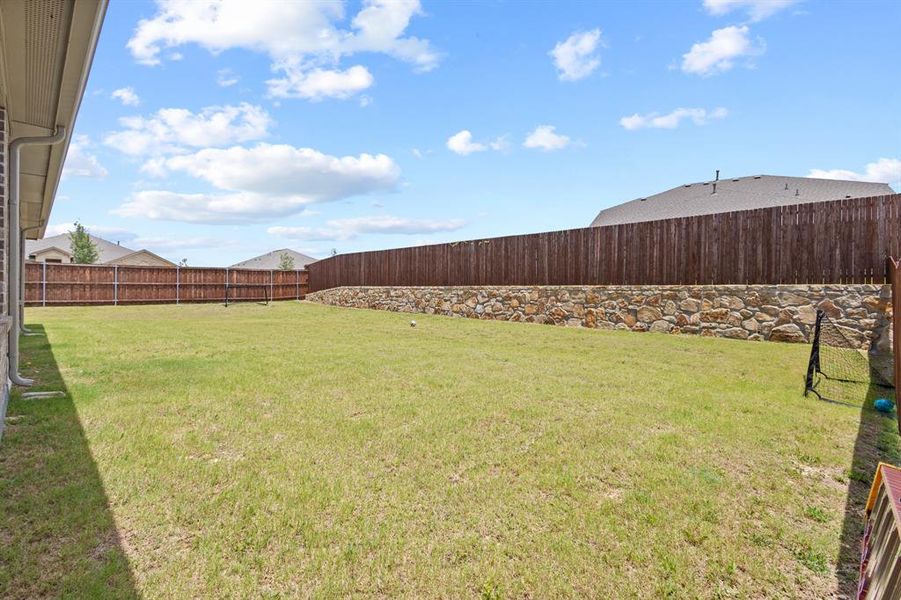 Spacious grassy yard featuring a stone retaining wall and a privacy fence Spacious grassy yard featuring a stone retaining wall and a privacy fence