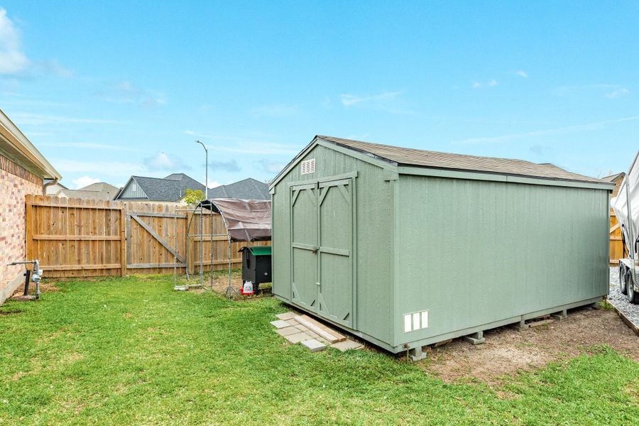 A spacious backyard features a well-maintained green lawn with a large, green storage shed 10x16. The area is enclosed by a wooden fence, providing privacy and a neat appearance. Perfect for storage or outdoor activities.
