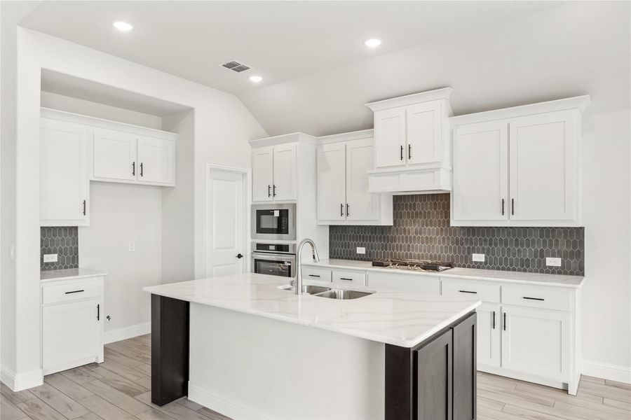 Kitchen with white cabinets, center island with sink, dark tile backsplash, and stainless steel appliances
