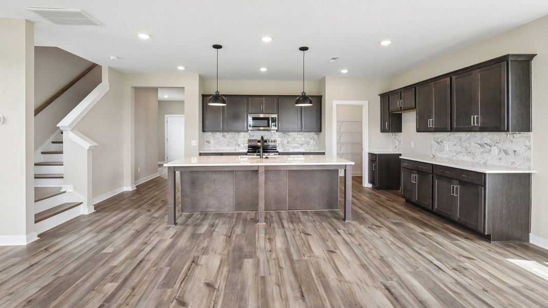 Kitchen with dark cabinetry, quartz countertops, and tile backsplash nearby staircase Kitchen with dark cabinetry, quartz countertops, and tile backsplash nearby staircase