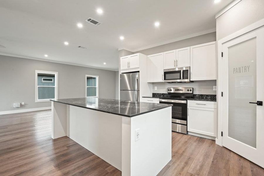 Kitchen featuring appliances with stainless steel finishes, recessed lighting, white cabinetry, dark stone counters, and light wood-style flooring