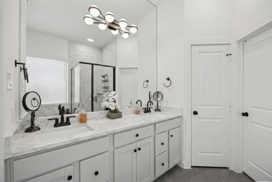 THE PRIMARY BATHROOM IS EQUIPPED WITH A DOUBLE VANITY, WHITE CABINETRY, AND A LARGE MIRROR WITH A MODERN LIGHT FIXTURE.