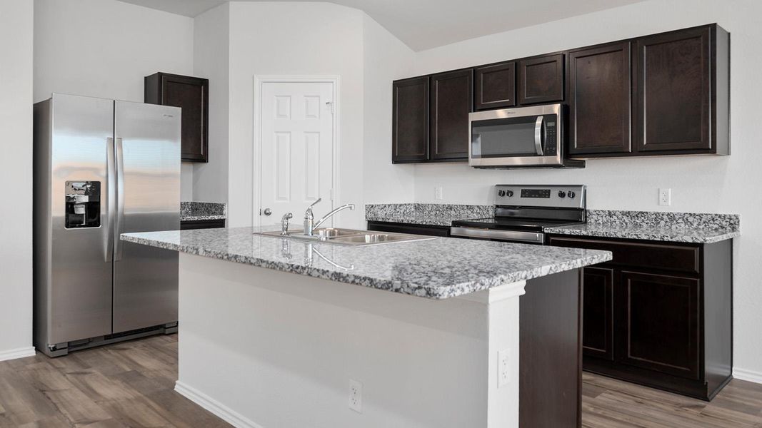 Kitchen with stainless steel appliances, dark brown cabinets, a kitchen island with sink, light stone counters, and dark wood finished floors
