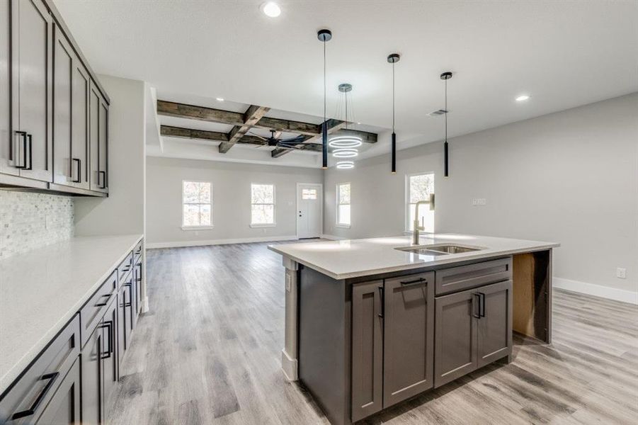 Kitchen featuring sink, coffered ceiling, light hardwood / wood-style flooring, pendant lighting, and a center island with sink