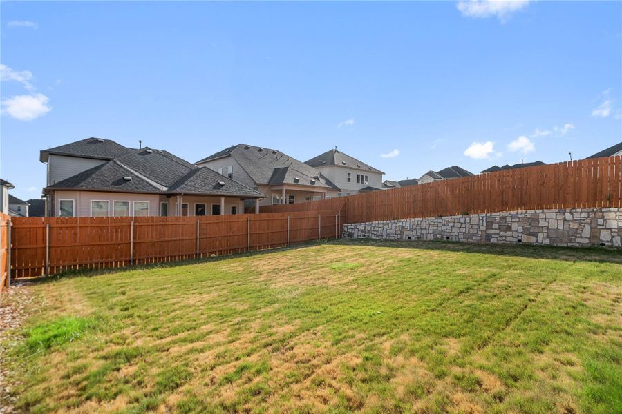 A spacious grassy lawn sits enclosed by tall wood fencing and a stone retaining wall.