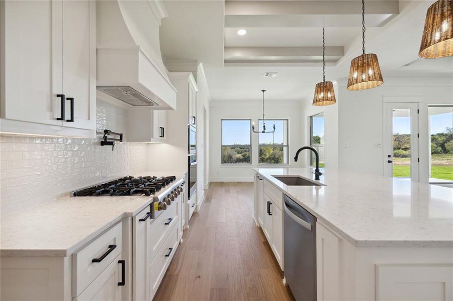 Kitchen featuring custom exhaust hood, stainless steel appliances, sink, decorative light fixtures, and white cabinetry