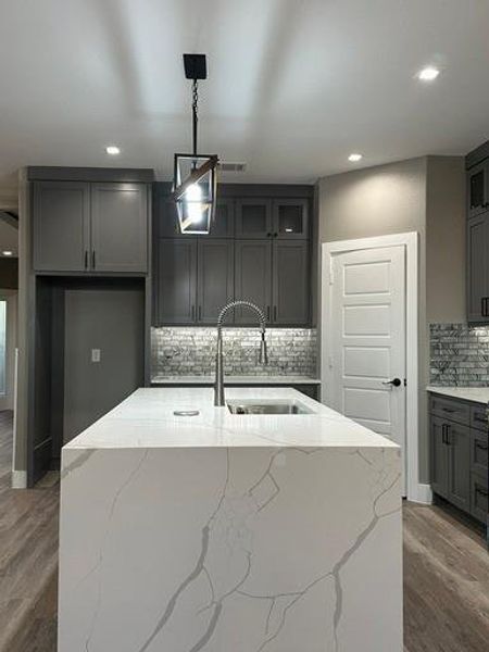 Kitchen with a center island with sink, pendant lighting, light stone counters, and sink