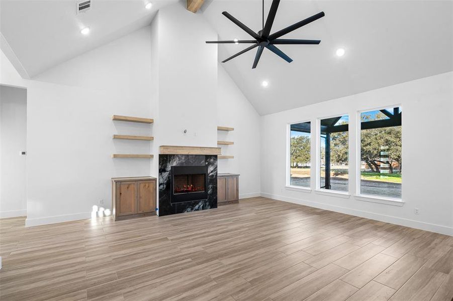 Unfurnished living room with a fireplace, high vaulted ceiling, ceiling fan, and beamed ceiling