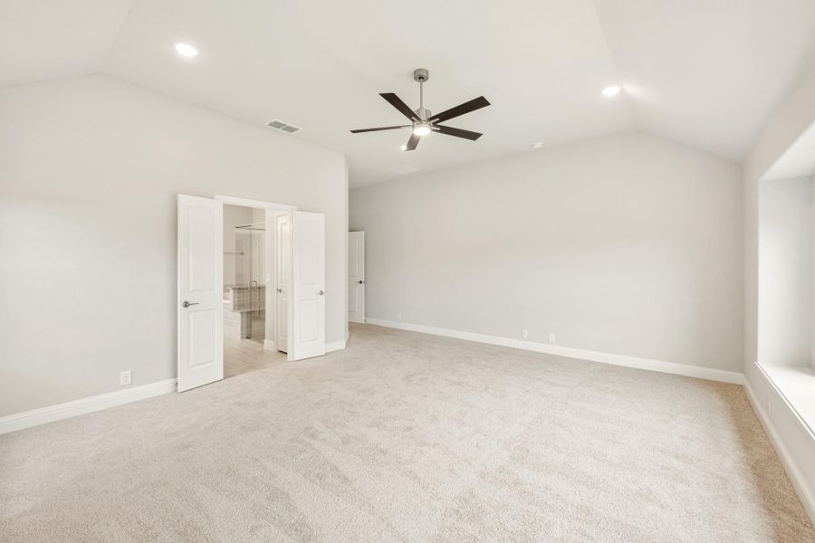 Spacious bedroom with vaulted ceiling, ceiling fan, carpet flooring, and open doors leading to ensuite bathroom.