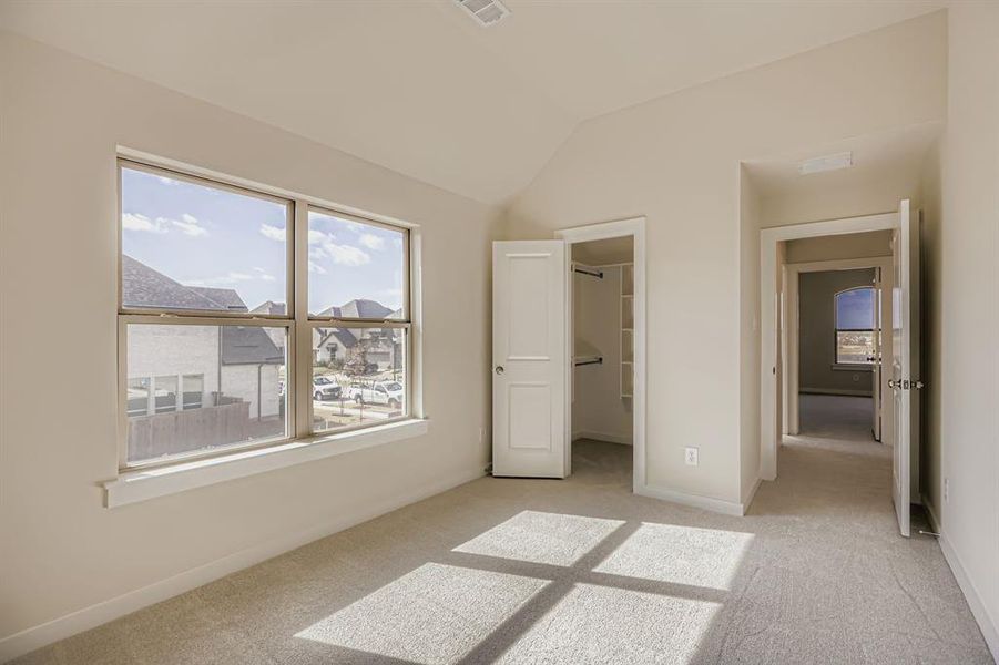 Unfurnished bedroom featuring light colored carpet, a walk in closet, and vaulted ceiling Unfurnished bedroom featuring light colored carpet, a walk in closet, and vaulted ceiling