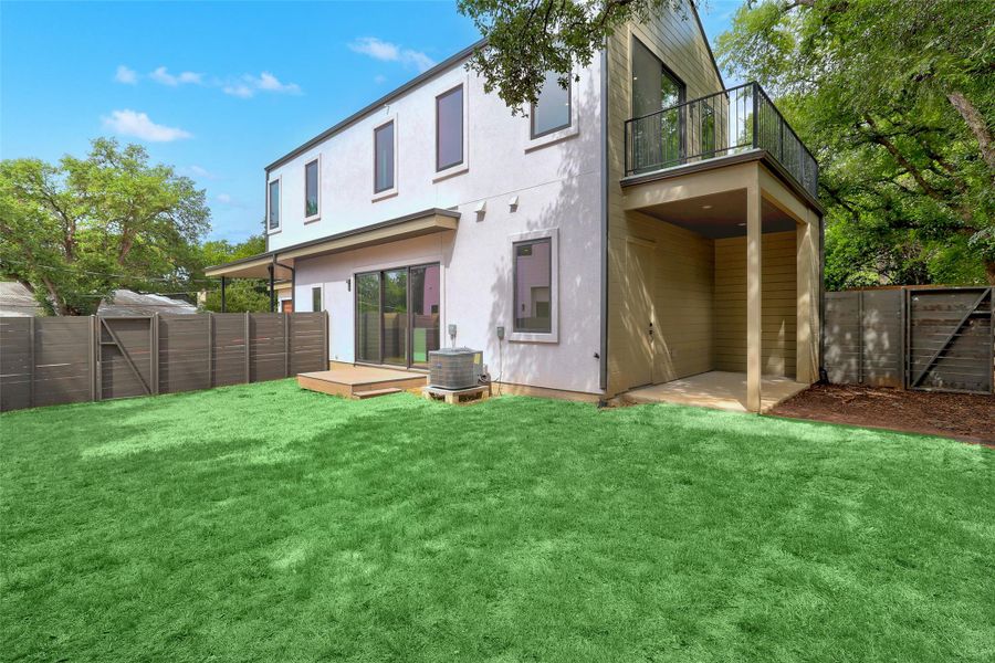 Back of property featuring a fenced backyard, a balcony, stucco siding, and a wooden deck