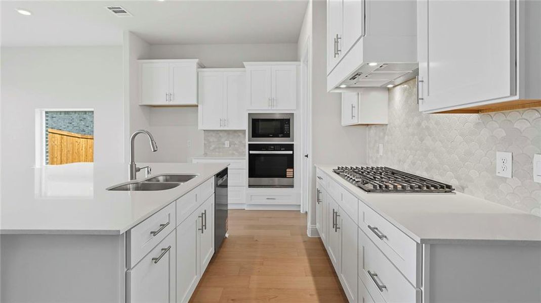 Kitchen with stainless steel appliances, an island with sink, backsplash, light wood-style flooring, and white cabinetry