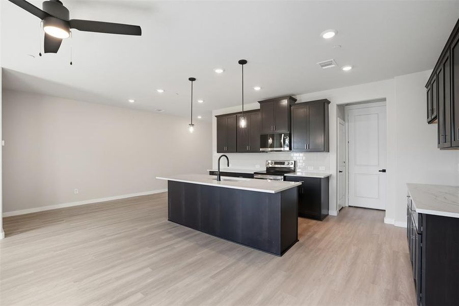 Kitchen featuring hanging light fixtures, an island with sink, backsplash, recessed lighting, and appliances with stainless steel finishes Kitchen featuring hanging light fixtures, an island with sink, backsplash, recessed lighting, and appliances with stainless steel finishes