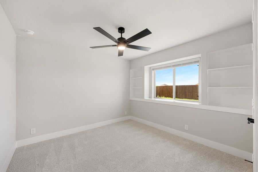 Empty bedroom with carpet, black ceiling fan, built-in shelves, and a window overlooking a wood fence yard. Empty bedroom with carpet, black ceiling fan, built-in shelves, and a window overlooking a wood fence yard.