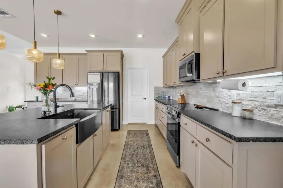 Kitchen with cream cabinets, stainless steel appliances, an island with sink, pendant lighting, and ornamental molding Kitchen with cream cabinets, stainless steel appliances, an island with sink, pendant lighting, and ornamental molding