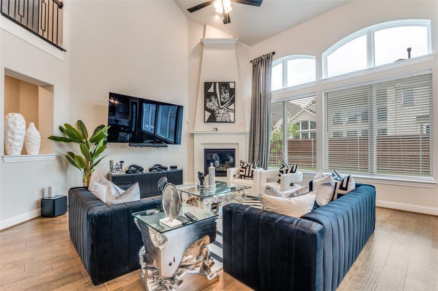 Living area with light wood-style flooring, a glass covered fireplace, high vaulted ceiling, and a ceiling fan