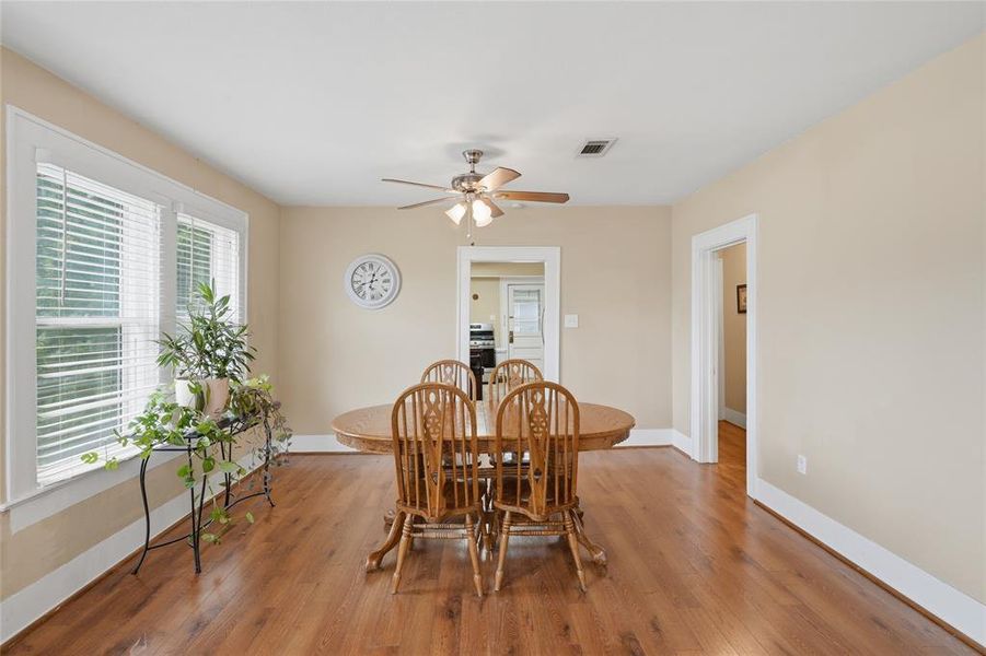Dining area featuring wood-finish flooring, multiple windows with blinds, a ceiling fan with integrated lighting, and neutral wall tones