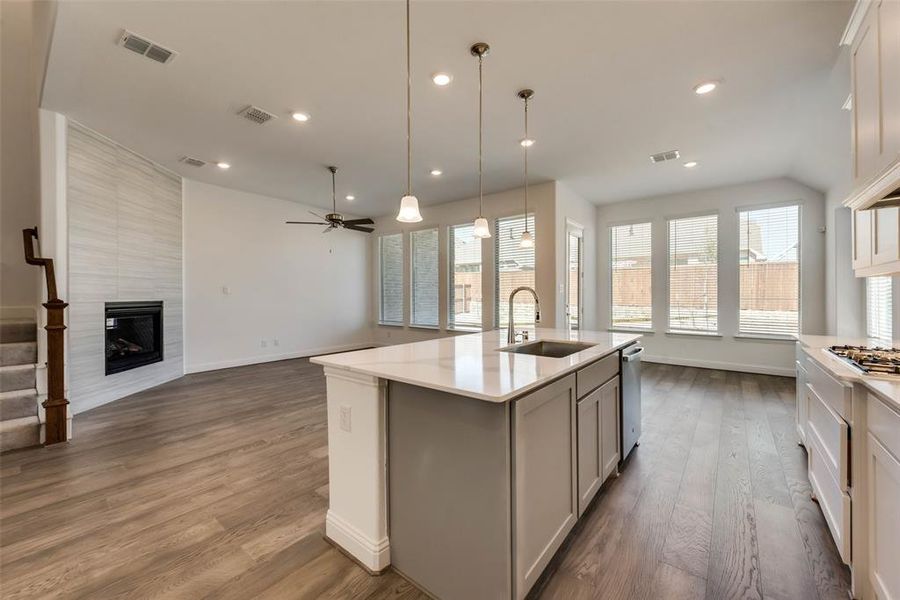 Kitchen with a kitchen island with sink, a tile fireplace, stainless steel appliances, sink, and wood-type flooring