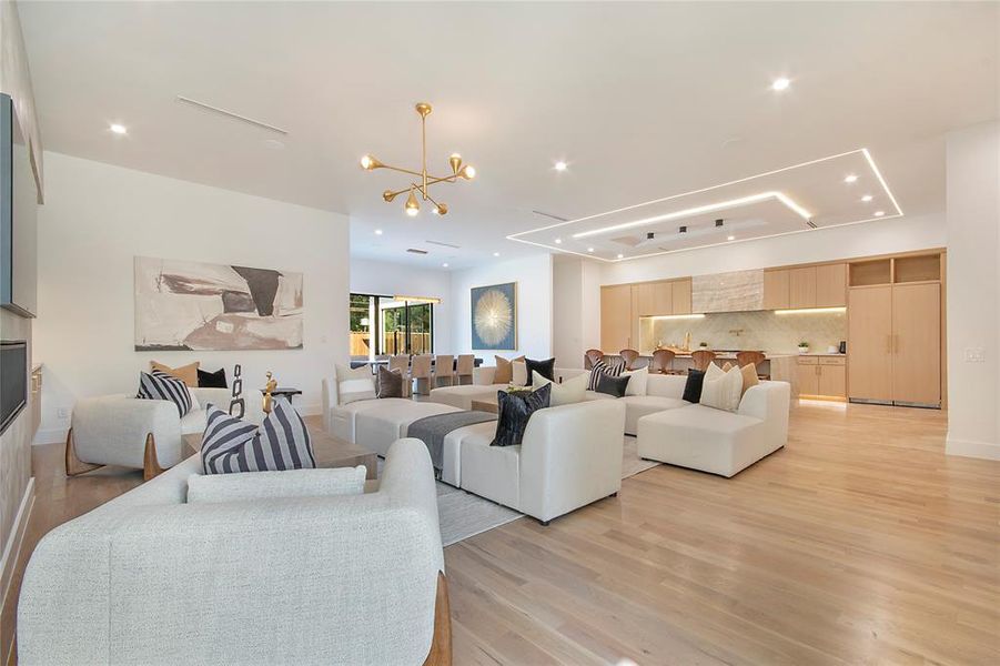 Living room with a chandelier, light wood-style flooring, recessed lighting, and a raised ceiling