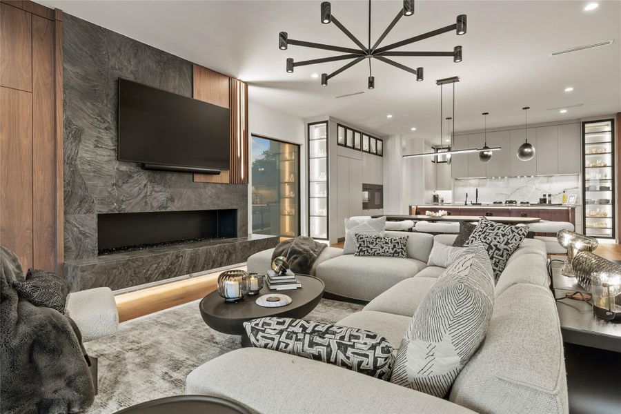 Open concept living area featuring a linear fireplace with a stone surround, integrated flat-screen television, and adjacent wood-paneling