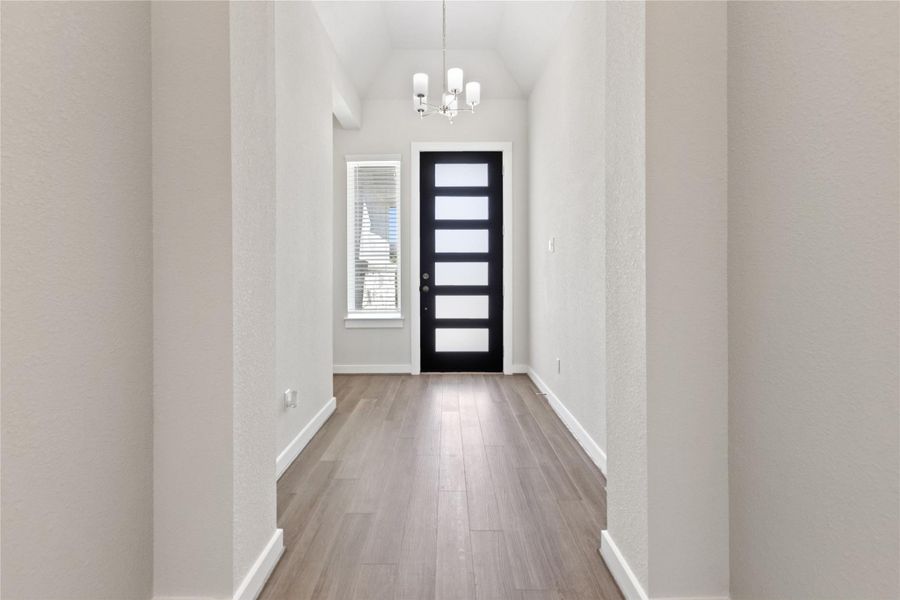 Foyer entrance featuring a chandelier, light wood-style flooring, lofted ceiling, and a textured wall