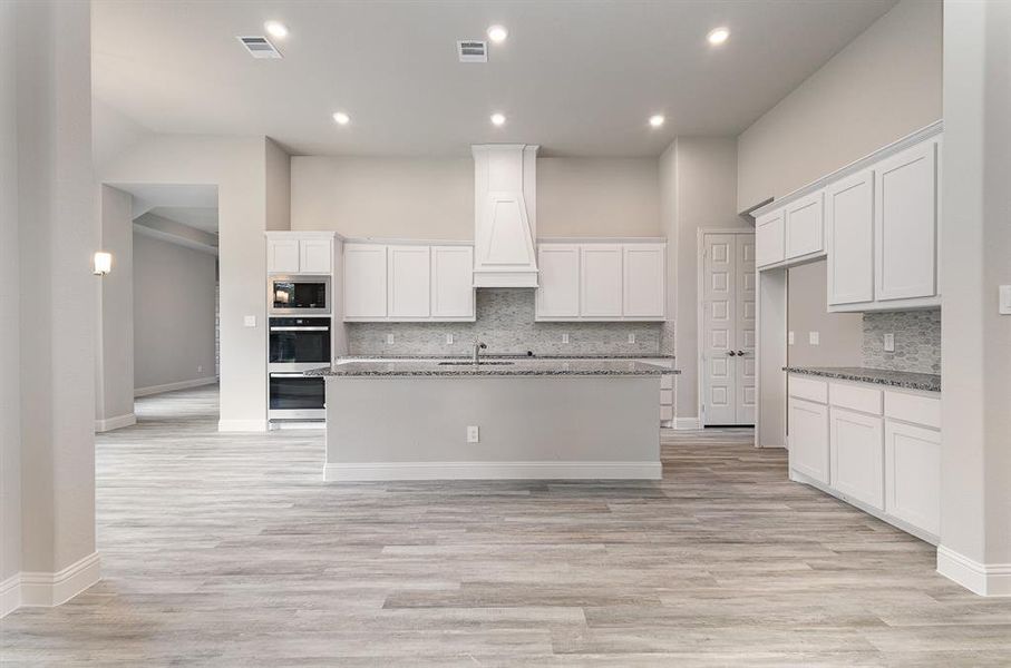 Kitchen with premium range hood, a center island with sink, white cabinets, dark stone countertops, and built in microwave