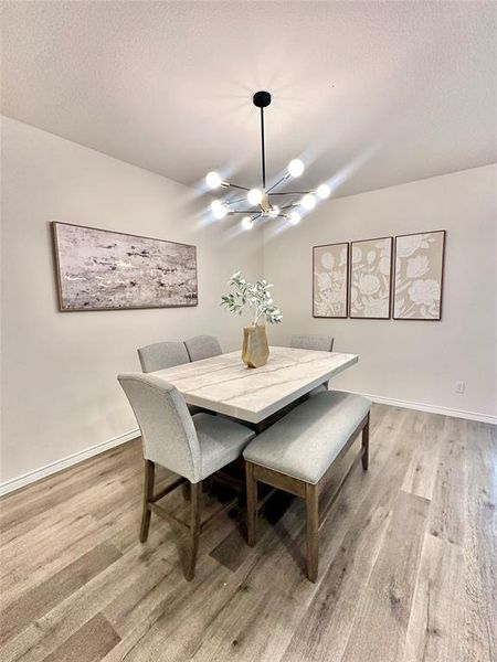 Dining room featuring a chandelier, a textured ceiling, and light wood-style flooring Dining room featuring a chandelier, a textured ceiling, and light wood-style flooring