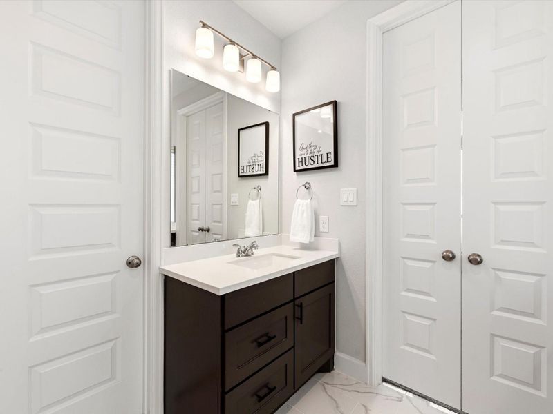 Clean, modern secondary vanity with a dark wood cabinet, white quartz countertop, and polished chrome fixtures. Features a large framed mirror, updated lighting, and neutral finishes that tie seamlessly into the primary bath design.