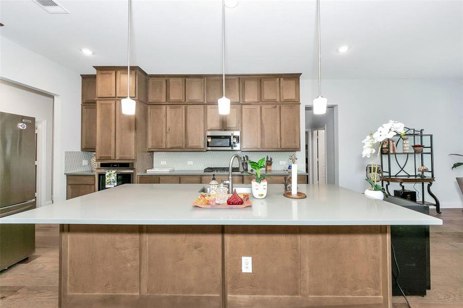 Kitchen with tasteful backsplash, a spacious island, pendant lighting, light hardwood / wood-style floors, and stainless steel appliances