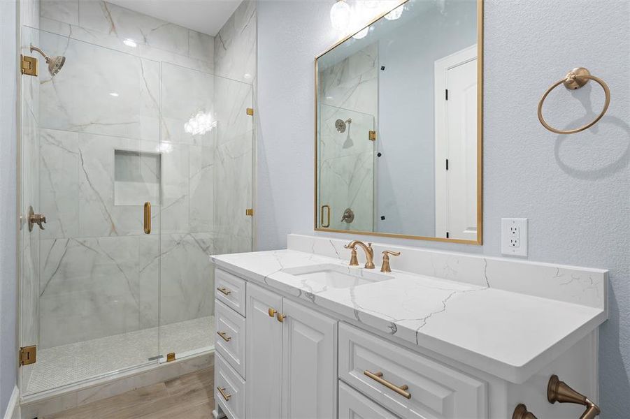 Bathroom with vanity, a marble finish shower, and a textured wall Bathroom with vanity, a marble finish shower, and a textured wall