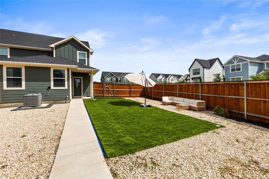 A well-maintained yard offers a concrete path leading to a private green space, enclosed by a sturdy wooden fence.