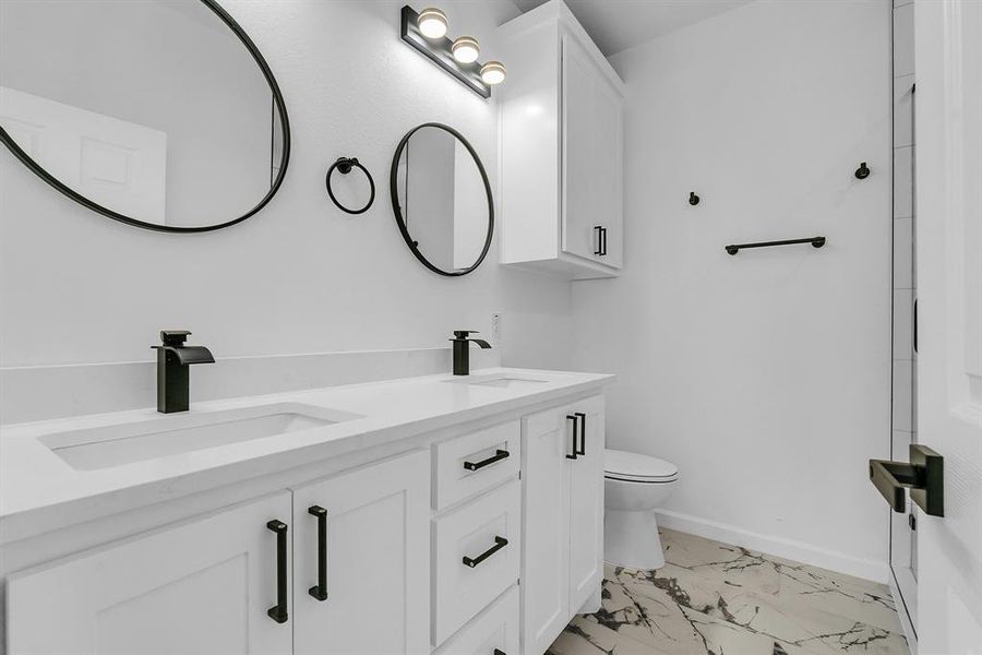 Bathroom with toilet, double sink vanity, and tile patterned floors