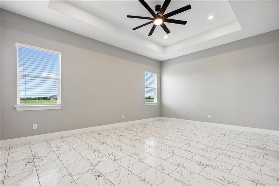 Spare room featuring a tray ceiling, baseboards, and ceiling fan